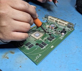 an image of a person soldering a board, holding a soldering iron in one hand and tweezers in the other